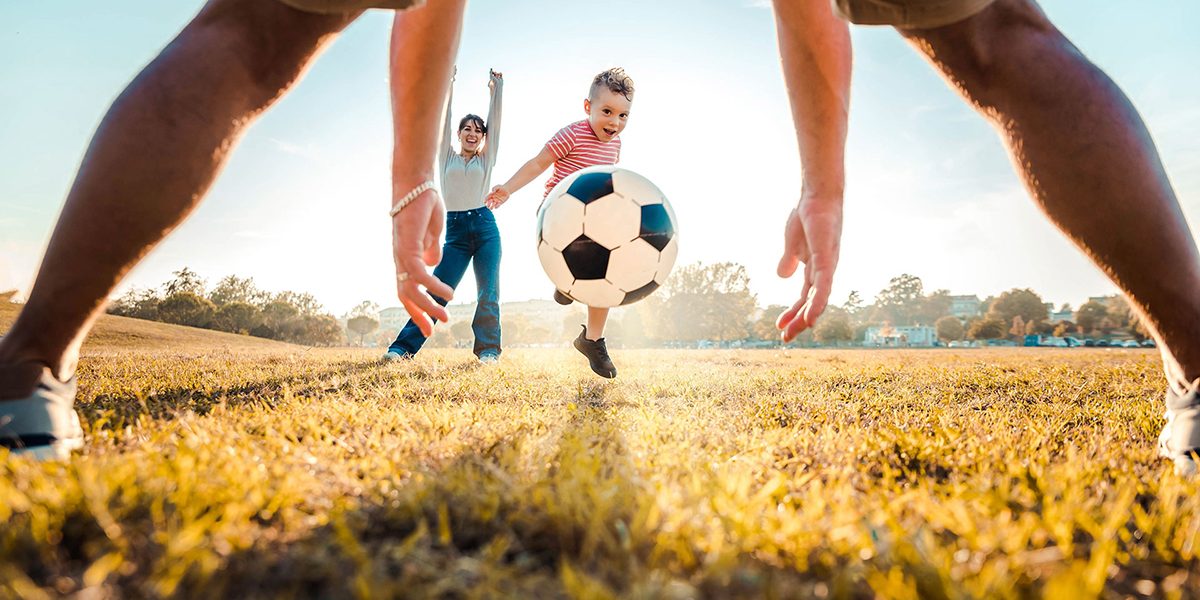 Kid kicking football ball while playing with his family - Active