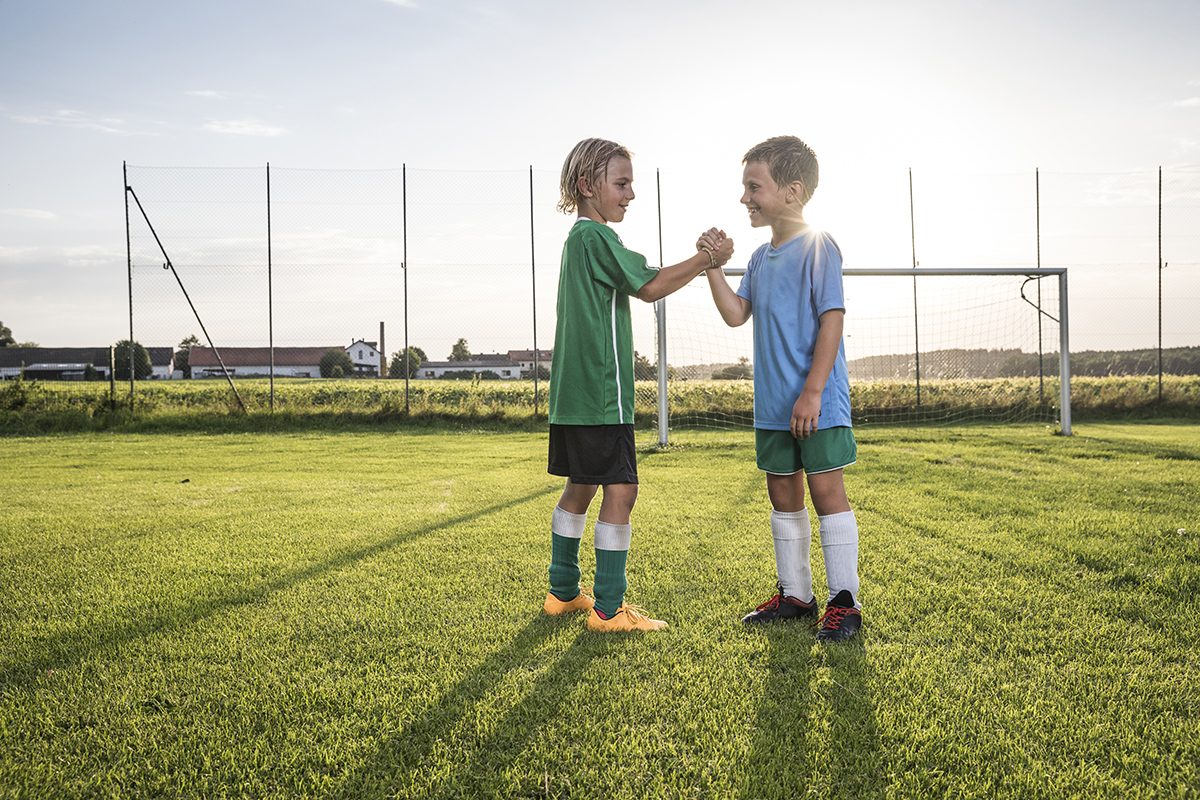 Smiling young football players shaking hands on football ground