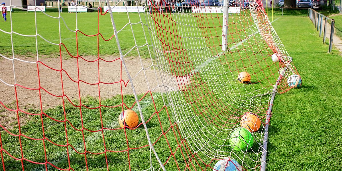 Many soccer balls in the net gate, equipment on green grass prepared for training in kids football academy. Health and active lifestyle. Popular sport activity